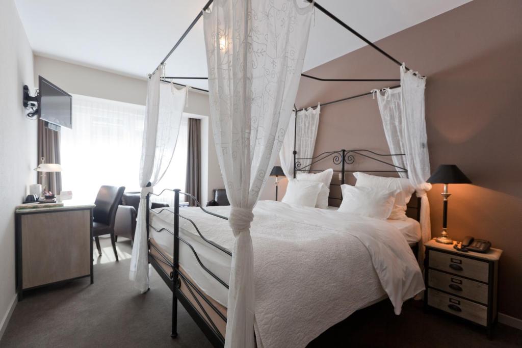 奥斯坦德德霍克美思酒店的一间卧室配有一张带白色寝具的天蓬床和一张书桌。