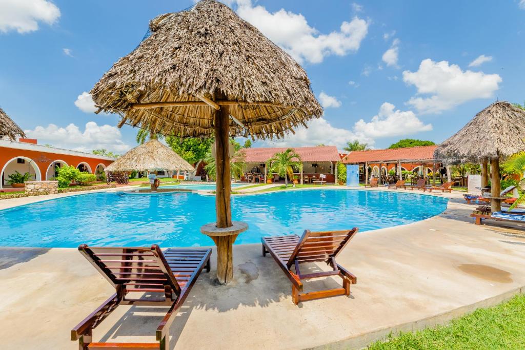 梅里达庄园酒店的一个带两把椅子和一把草伞的度假游泳池