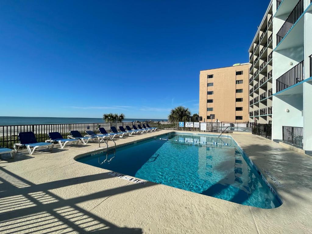 默特尔比奇Polynesian Oceanfront Hotel的一个带椅子的游泳池,背景是大海