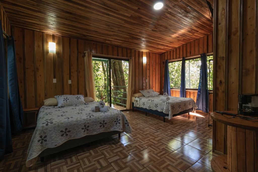 蒙泰韦尔德哥斯达黎加The Green Tree Lodge的一间带两张床铺的卧室,位于带木墙的房间内
