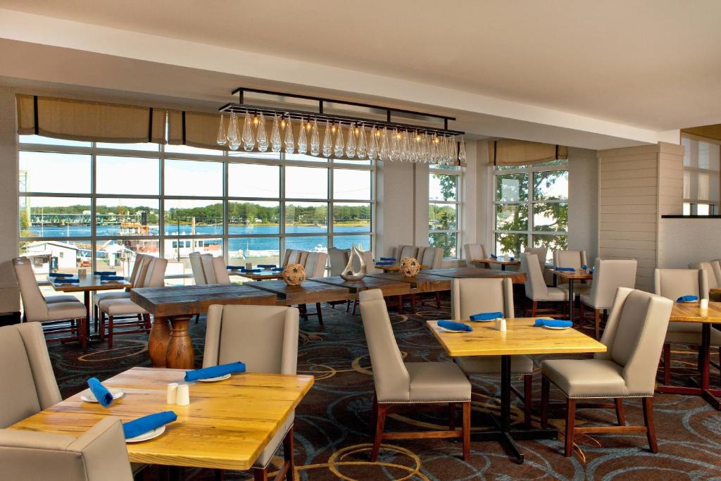 朴茨茅斯朴茨茅斯哈勃尔赛德喜来登酒店的餐厅设有木桌、椅子和大窗户。