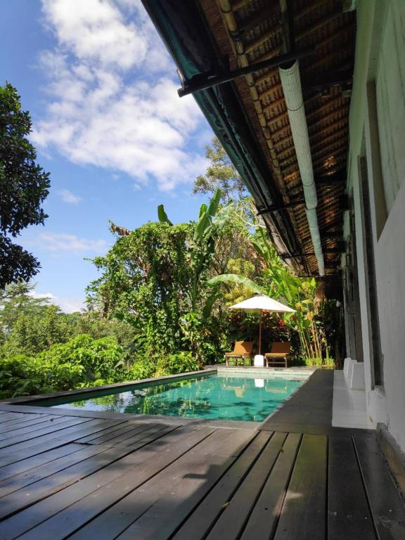 乌布Villa Damai Shanti的一个带木制甲板和遮阳伞的游泳池