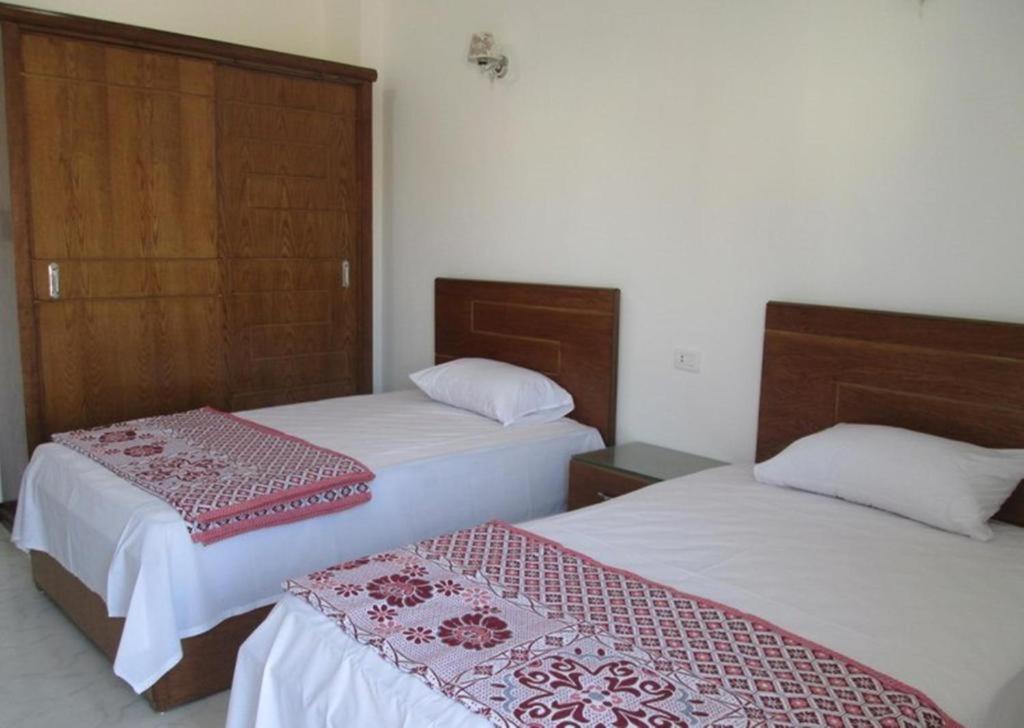 Jazīrat al ‘AwwāmīyahNile Paradise的一间卧室配有2张带白色床单和红色点缀的床。