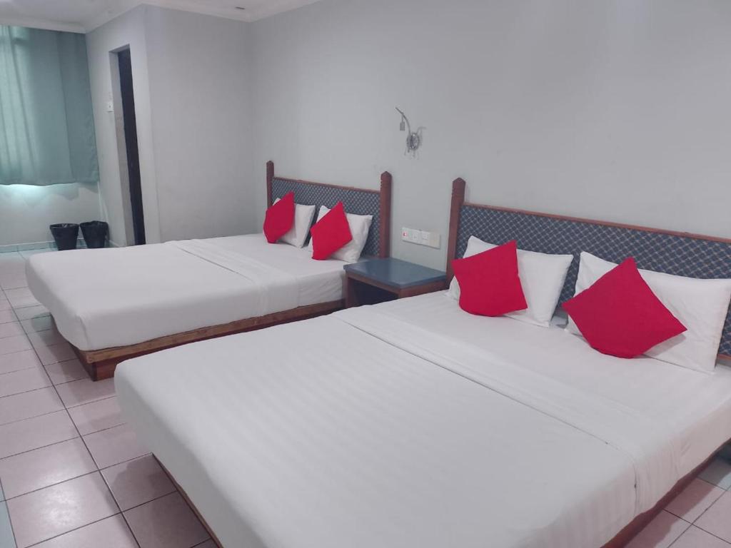 MukahHighway Inn的两张位于酒店客房的床铺,配有红色枕头