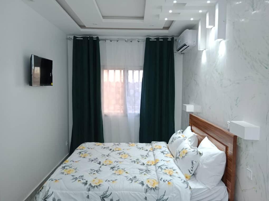达喀尔Studio Emeraude - cosy et climatisé - Résidence Saraba Mermoz的一间卧室设有床铺和一个带绿色窗帘的窗户。