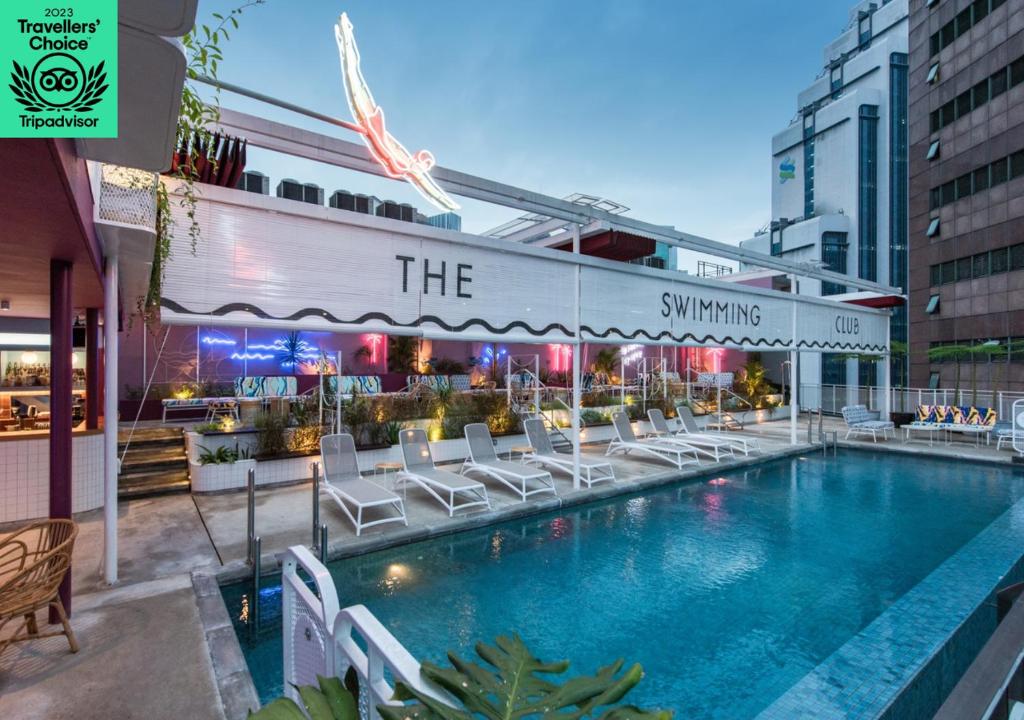 吉隆坡吉隆坡杂志酒店的一座带白色椅子的游泳池,位于大楼旁