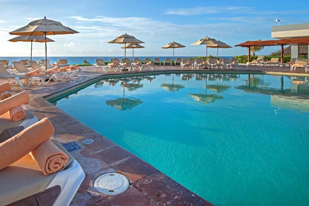 坎昆Park Royal Beach Cancun - All Inclusive的一个带椅子和遮阳伞的游泳池以及大海