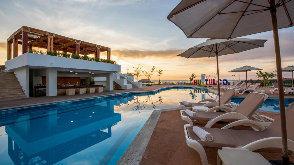 圣克鲁斯华特库Park Royal Beach Huatulco - All Inclusive的酒店前方的游泳池配有椅子和遮阳伞