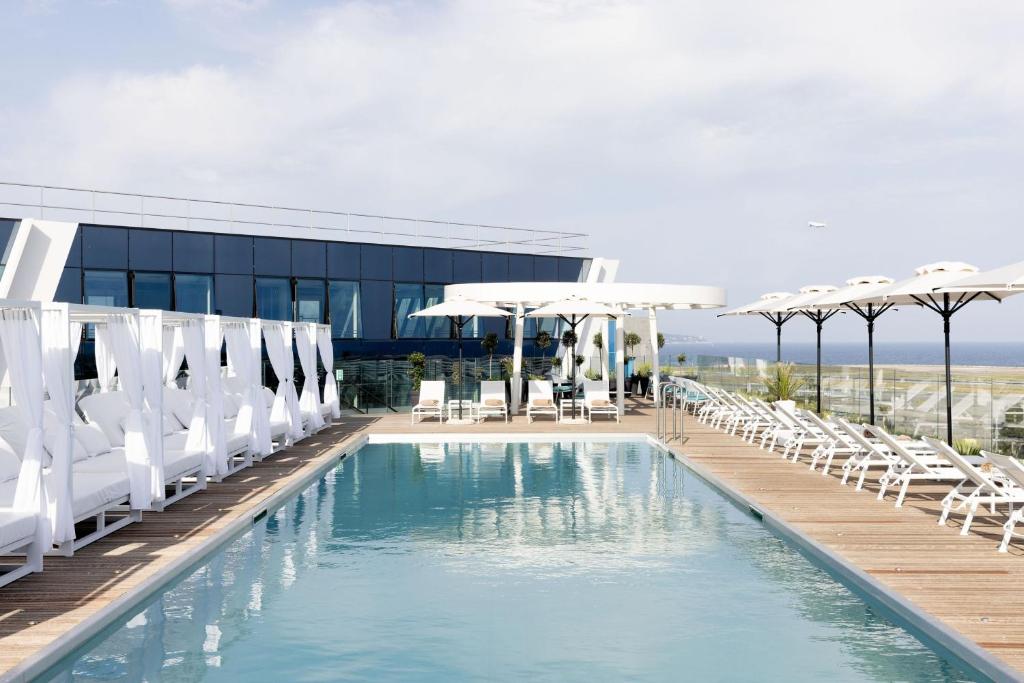 尼斯Sheraton Nice Airport的一个带白色椅子和遮阳伞的游泳池