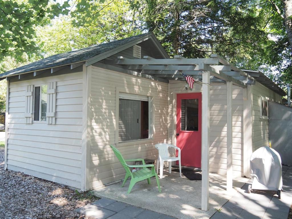 HonorSleeping Bear Riverside Cabins - Cabin #4的白色的棚子,有红色的门和绿色的椅子