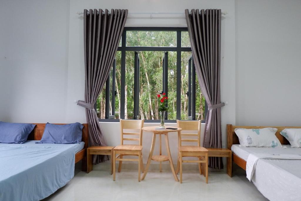 Hồ ÐáHương Tràm的客房设有两张床、一张桌子、椅子和窗户。