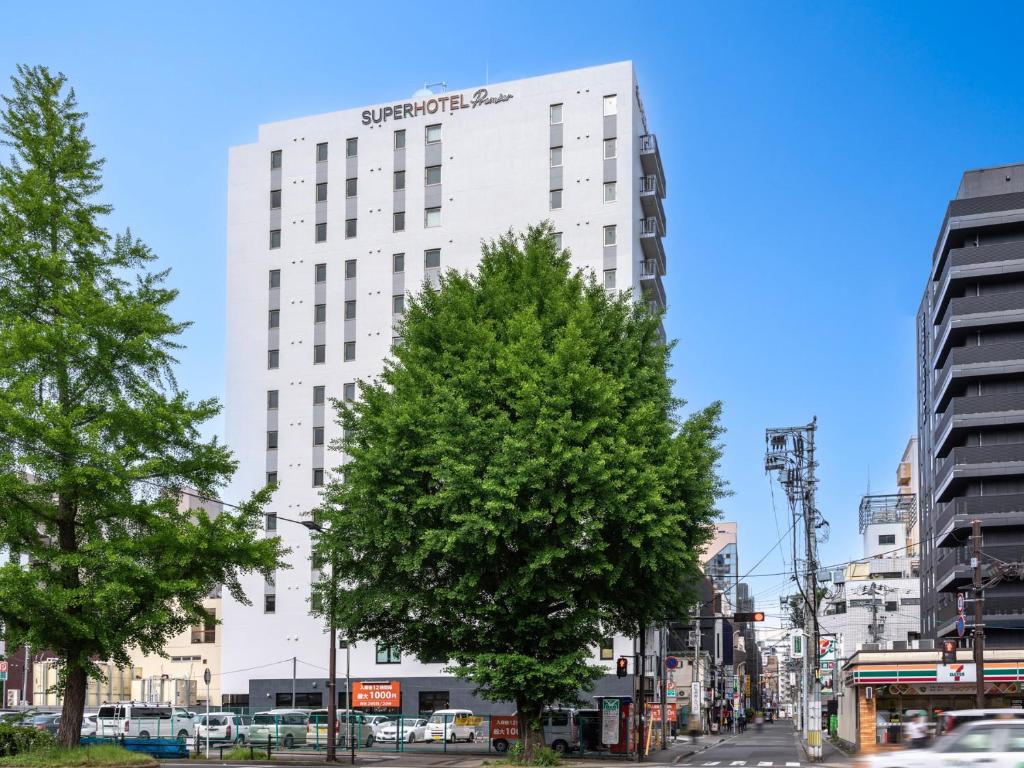 仙台Super Hotel Premier Sendai Kokubuncho Tennenonsen的一座高大的白色建筑,前面有一棵树