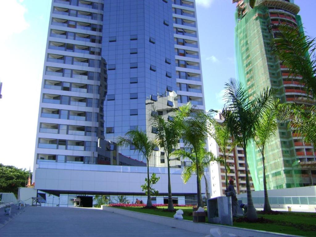 累西腓Boa Viagem 420 Apart Hotel的一座棕榈树环绕的建筑,位于高楼前