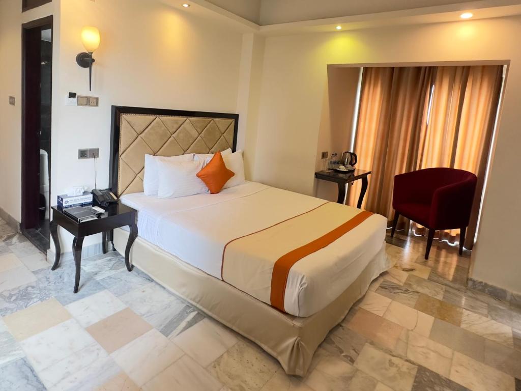 达卡The Elite Residence Dhaka的一间卧室配有一张大床和一张红色椅子