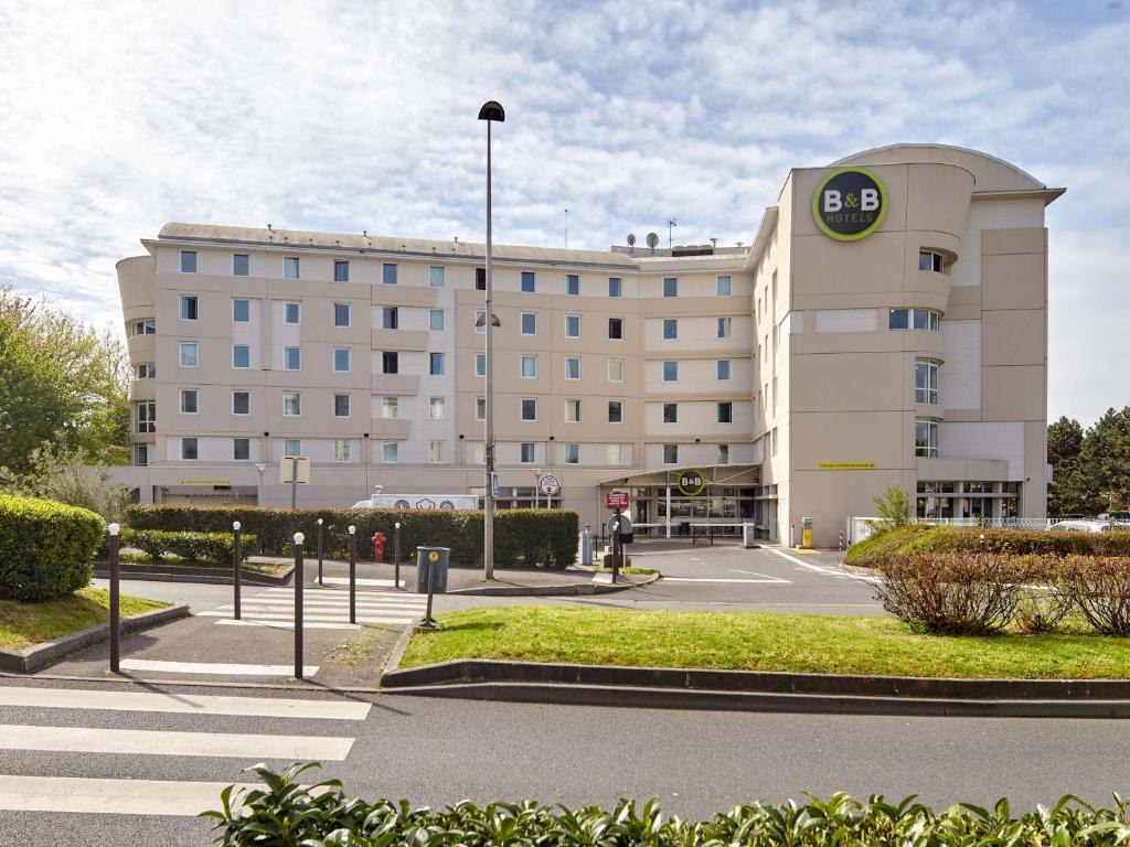 鲁瓦西昂法兰西B&B HOTEL Paris Roissy CDG Aéroport的一座大型建筑,前面设有停车场