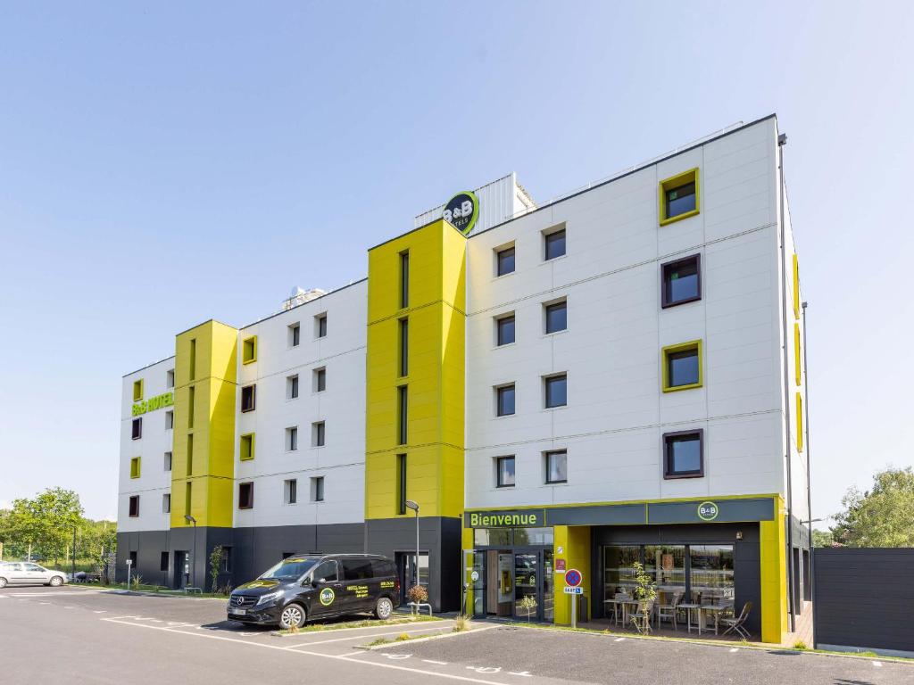 布吕兹B&B HOTEL Rennes Parc Expo Aéroport的白色和黄色的建筑,停车场有停车位