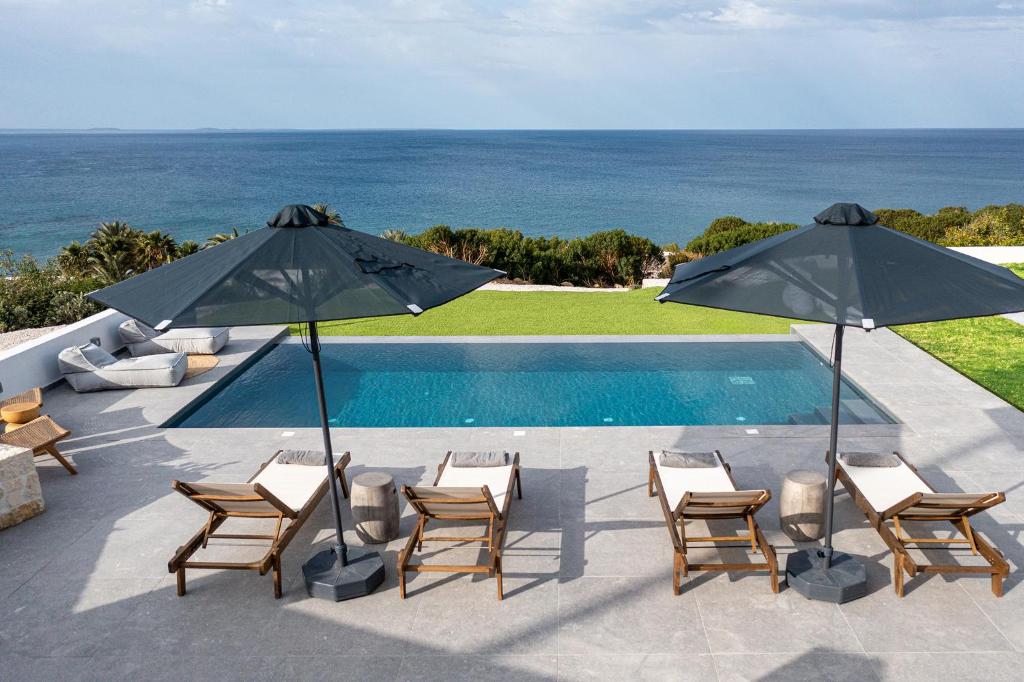 依拉佩特拉Nouvelle Villa的毗邻大海的带椅子和遮阳伞的游泳池