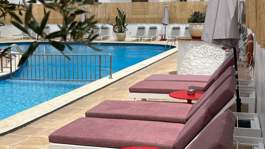 圣安东尼奥Aparthotel Boutique Poniente Playa的一个带2把躺椅和桌子的游泳池