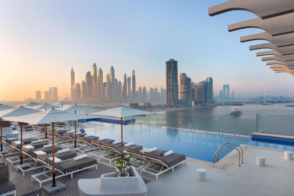 迪拜voco Dubai The Palm, an IHG Hotel的一个带椅子和遮阳伞的游泳池以及一个城市