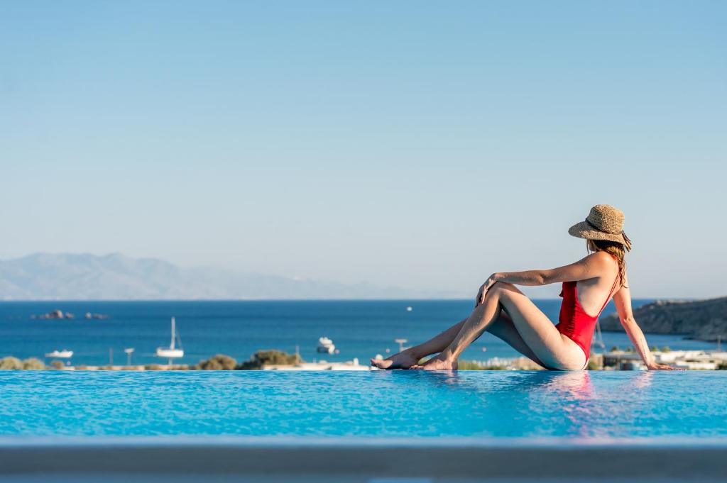 凯勒里瓦迪Mykonos4Islands Seaside Apartments的坐在海滩水面上的一个戴帽子的女人