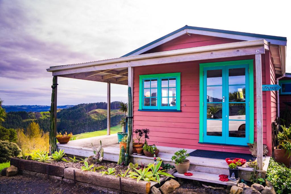 拉格伦Fridas Accommodation的一间粉红色的小房子,拥有蓝色的窗户和植物