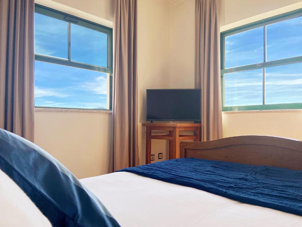 维尼艾什Vinhais Hotel的一间卧室设有一张床、一台电视和两个窗户。