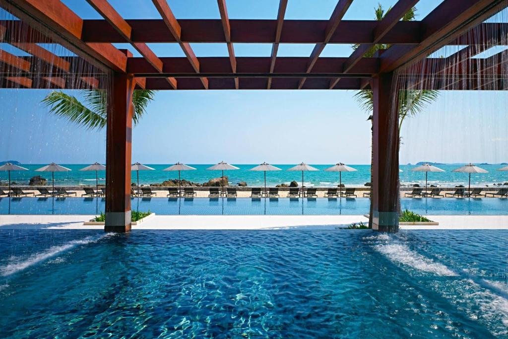 港生Rayong Marriott Resort & Spa的一座带遮阳伞的游泳池,其背景是大海