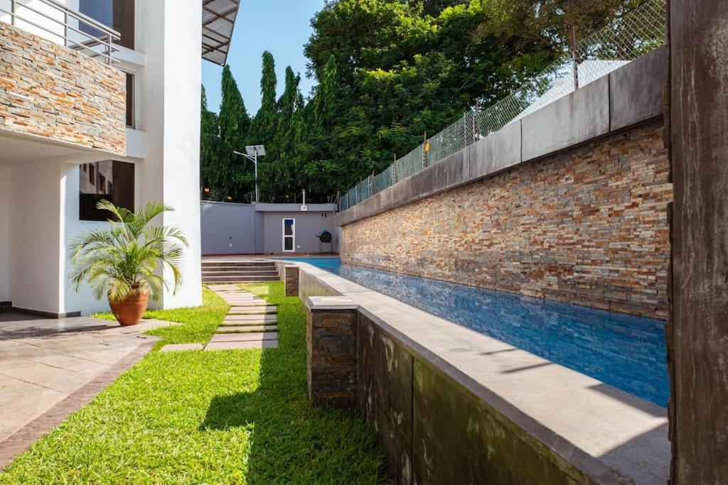 阿克拉Luxurious and peaceful 3BR Apt with a Pool Close to shops, restaurants, Kotoka Airport的砖墙,旁边是一座房子,设有游泳池