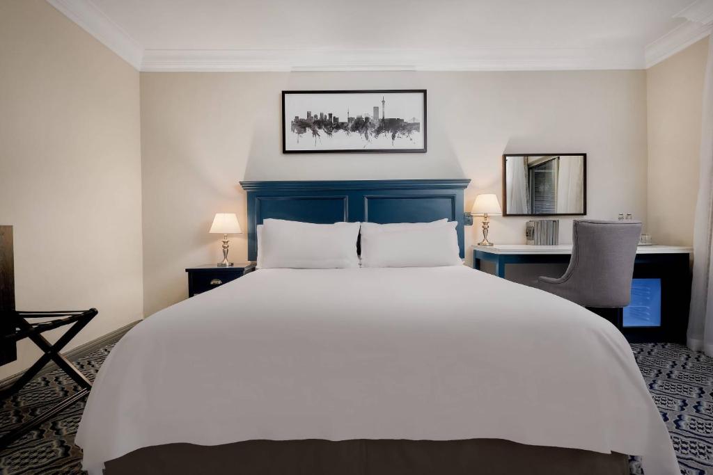 约翰内斯堡约翰内斯堡桑顿三角琴万豪Protea酒店的卧室配有一张白色大床和两把椅子