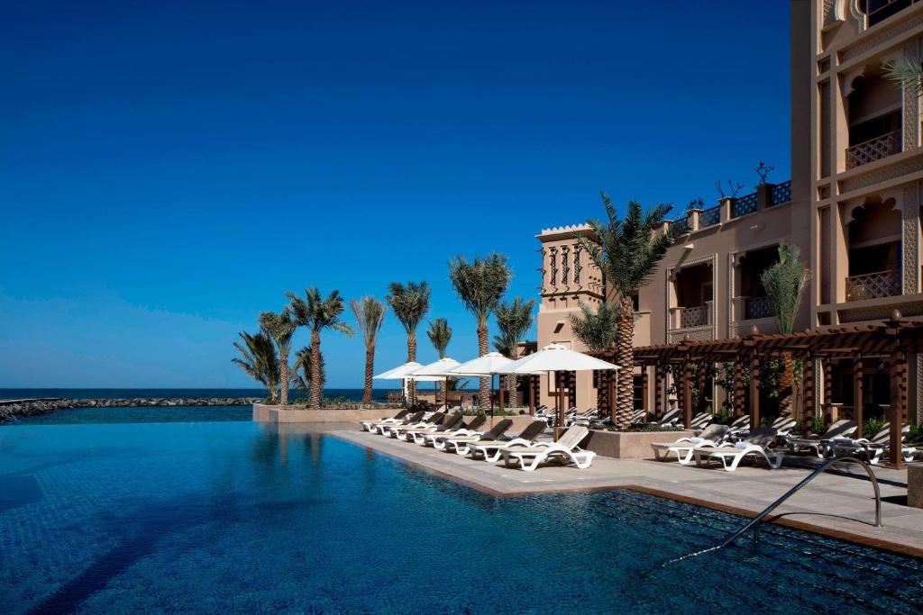 沙迦沙迦海滩喜来登Spa度假酒店的度假村的游泳池,配有椅子和遮阳伞
