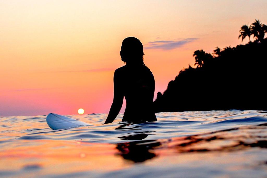 埃斯孔迪多港Secret Beach Hostel的日落时坐在海上冲浪板上的女人