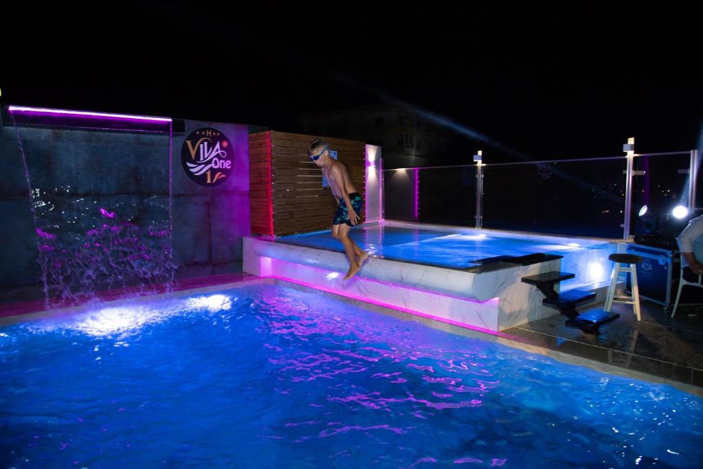 都拉斯Vila One Beach Hotel的男人在晚上跳进游泳池