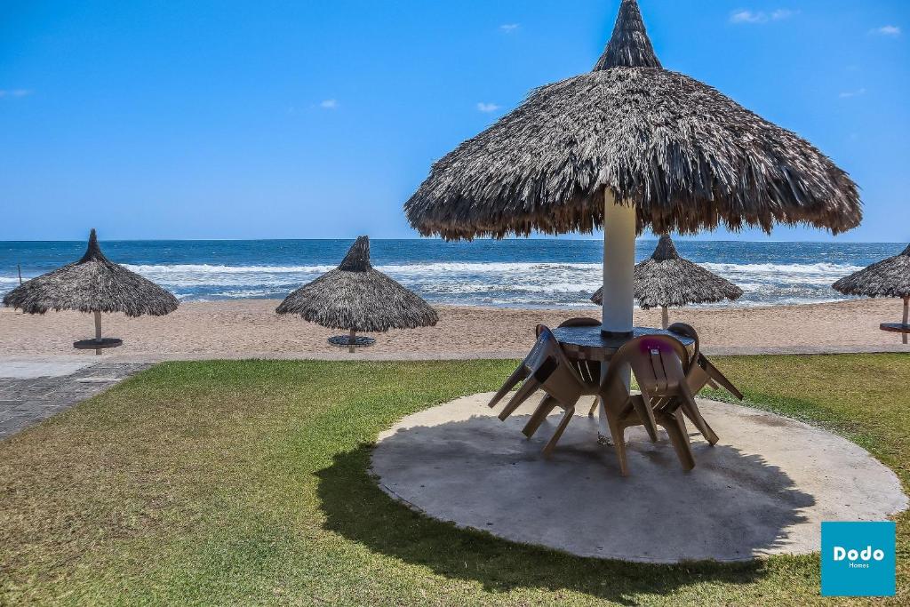 马萨特兰Departamento en Mazatlan con acceso a la playa y alberca común #138的海滩上遮阳伞下的桌椅