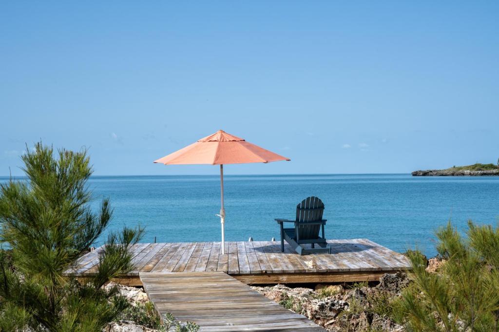 总督港Chez Cay Cottage cottage的一把椅子,坐在带雨伞的码头上