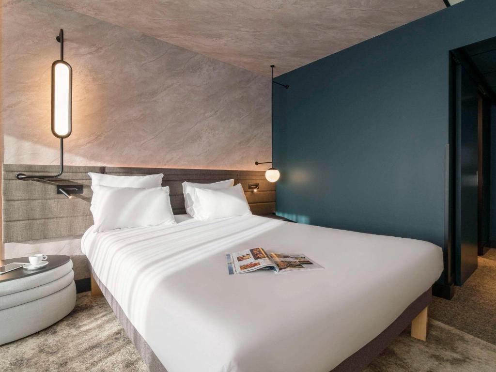 鹿特丹鹿特丹布莱恩诺富特酒店的卧室配有一张大白色床,上面有杂志
