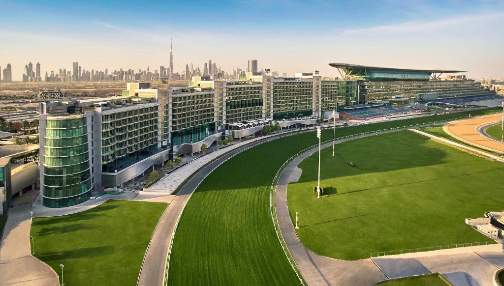 迪拜The Meydan Hotel Dubai的一座大建筑,在城市前方有绿色草坪