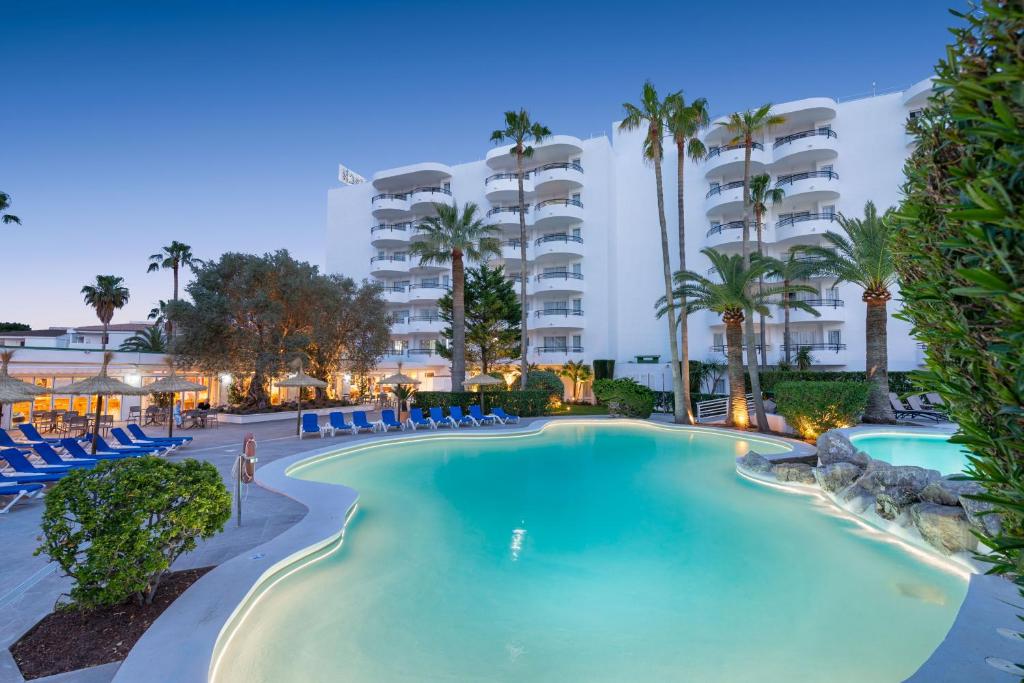 阿尔库迪亚港Alcudia Beach Apartments的棕榈树和椅子的度假村的游泳池