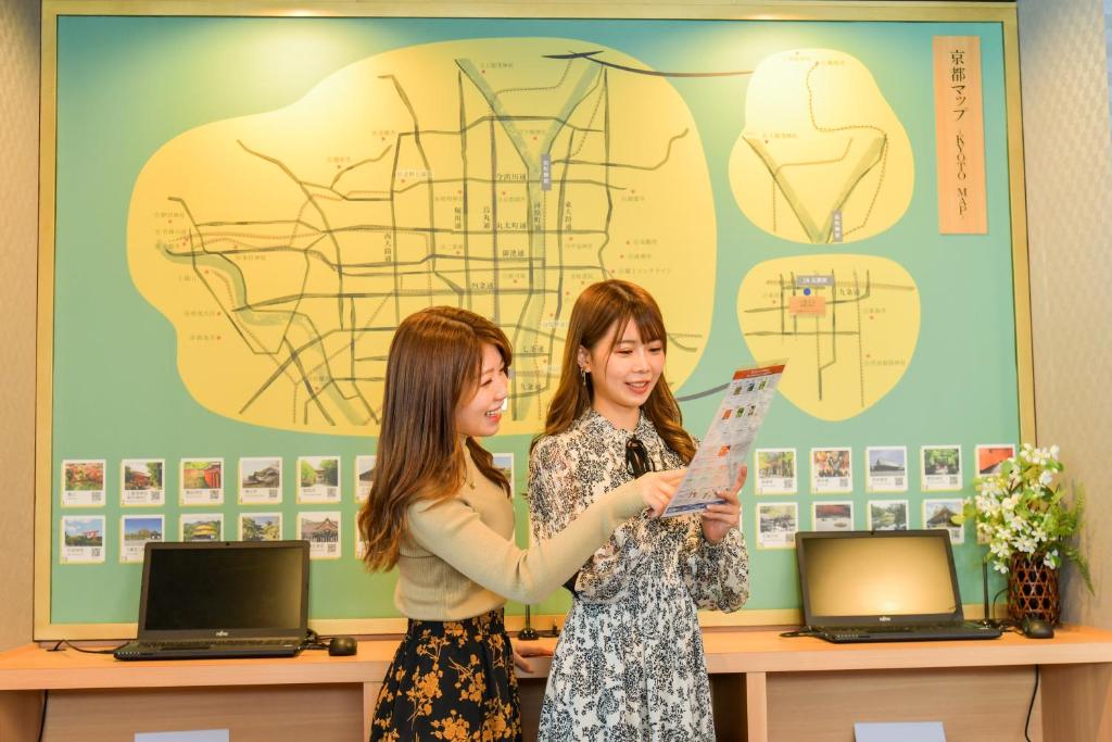 京都Sanco Inn Kyoto Hachijoguchi Shikinoyu的两个女人站在一个拿着一张纸的房间