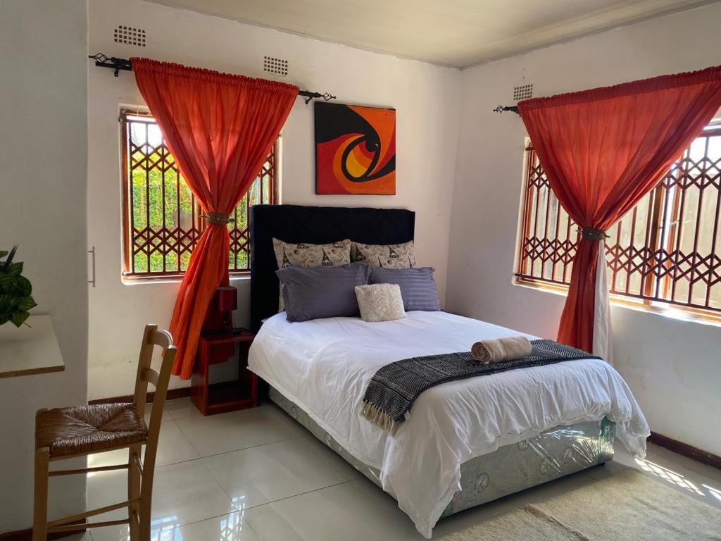 卢萨卡Samkab Legacy & comfort Ndeke (airport)的一间卧室配有一张带红色窗帘的床和一把椅子