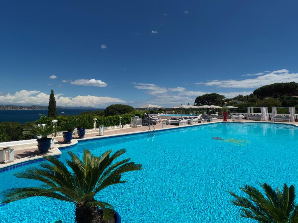 圣特罗佩Althoff Hotel Villa Belrose的一座大型蓝色游泳池,游泳池内种植了棕榈树,配有椅子