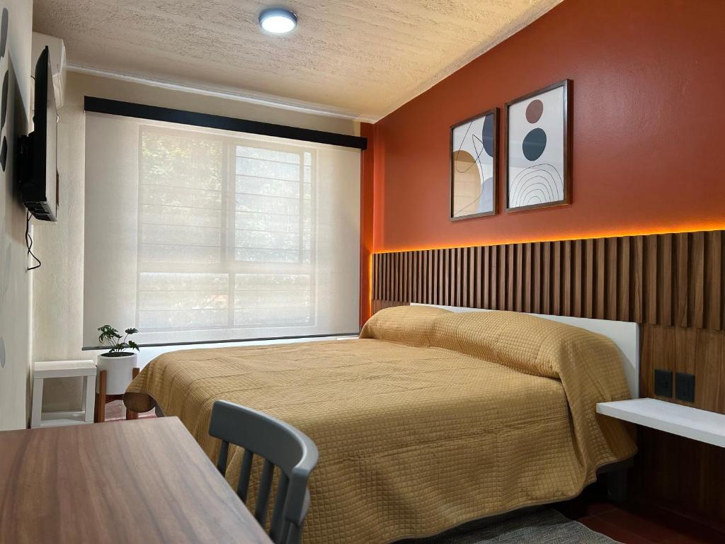 瓦哈卡市Xochimilco Apartment的一间卧室设有橙色的墙壁、一张床和一张桌子