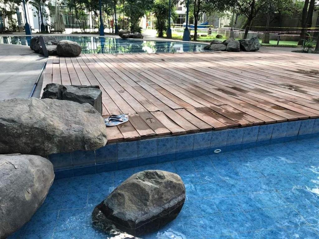 马尼拉Kasara Urban Resort and Residences的一个带岩石和木甲板的游泳池