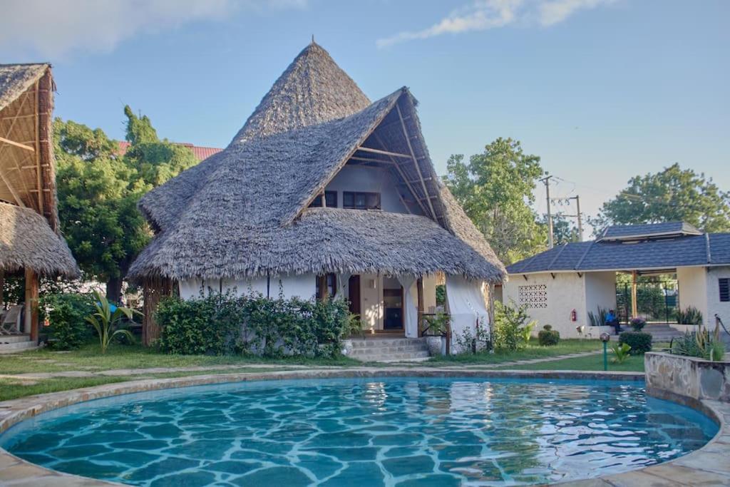 马林迪Cosy Cottage Marine Park at Malindi beach的茅草屋顶和游泳池的房子