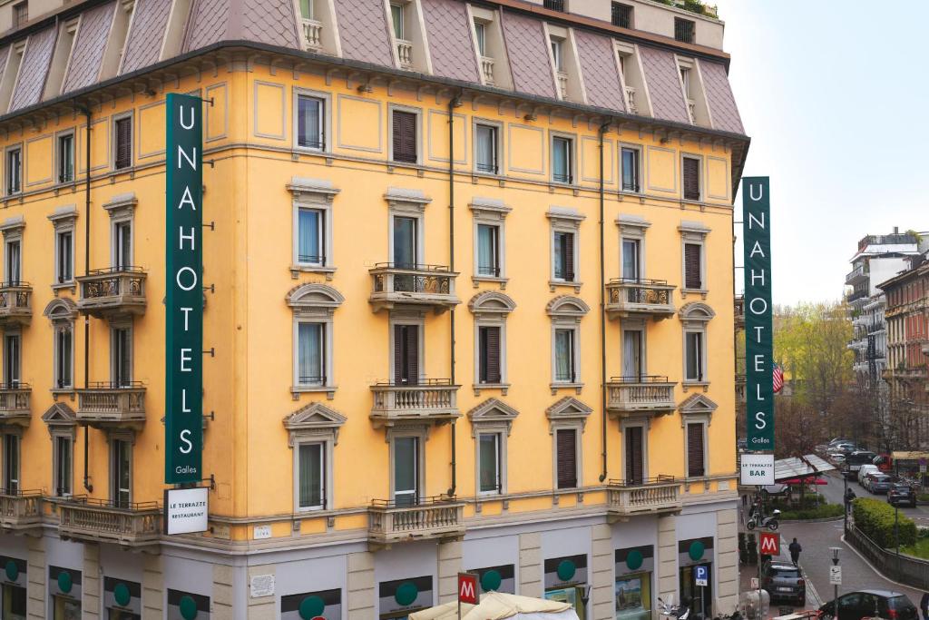 米兰UNAHOTELS Galles Milano的黄色的建筑,旁边标有标志