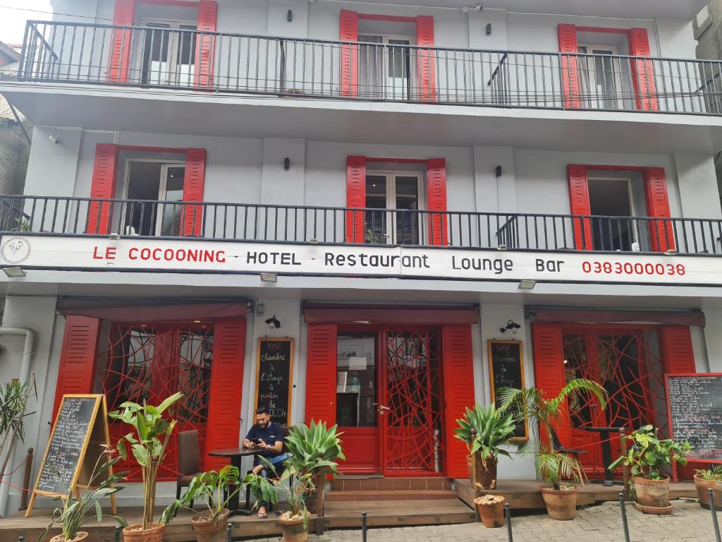 塔那那利佛Le Cocooning 974 Hôtel Restaurant Réunion的坐在红色建筑前面的人