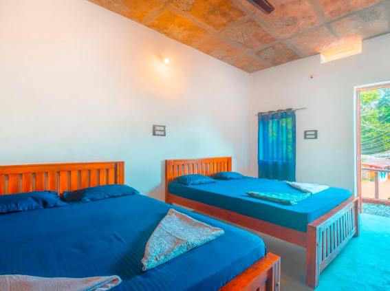 戈卡尔纳Taya Beach Front的卧室设有两张床,配有蓝色的床单和窗户。