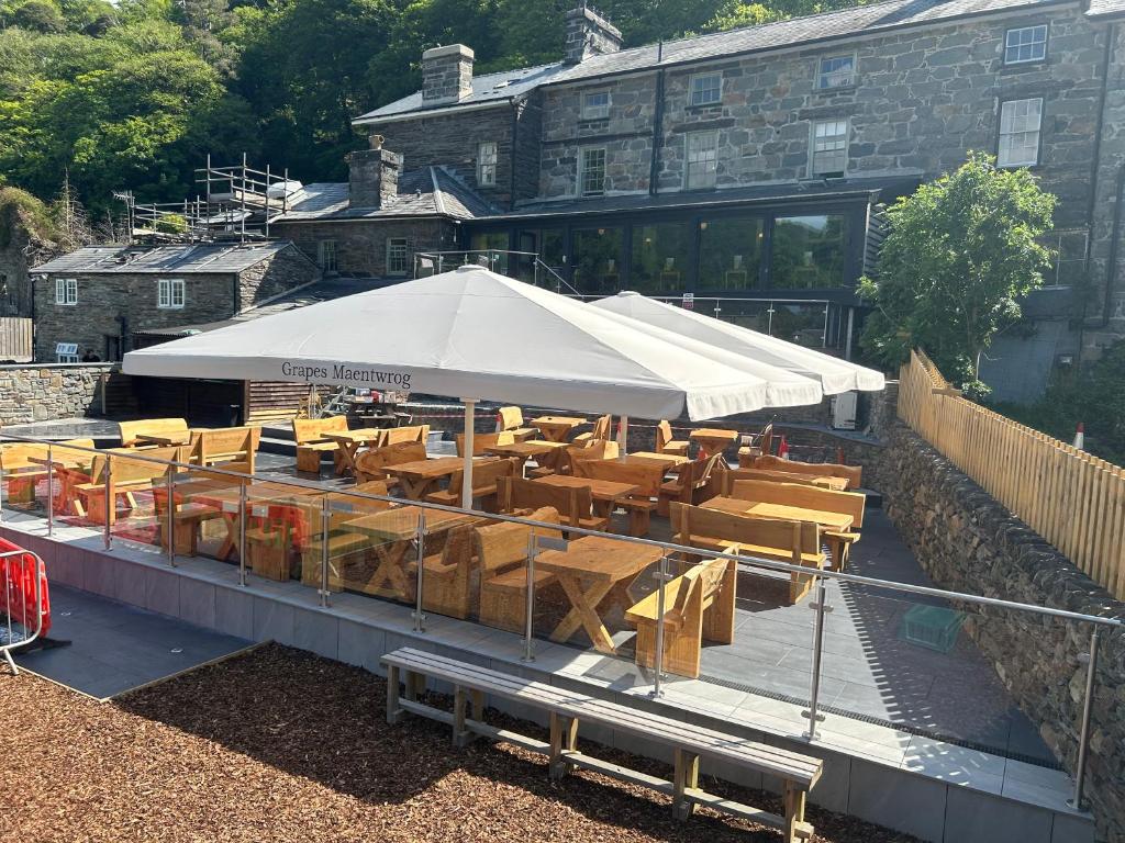 布莱奈费斯蒂尼奥格Grapes Hotel, Bar & Restaurant Snowdonia Nr Zip World的餐厅设有木桌和白色遮阳伞