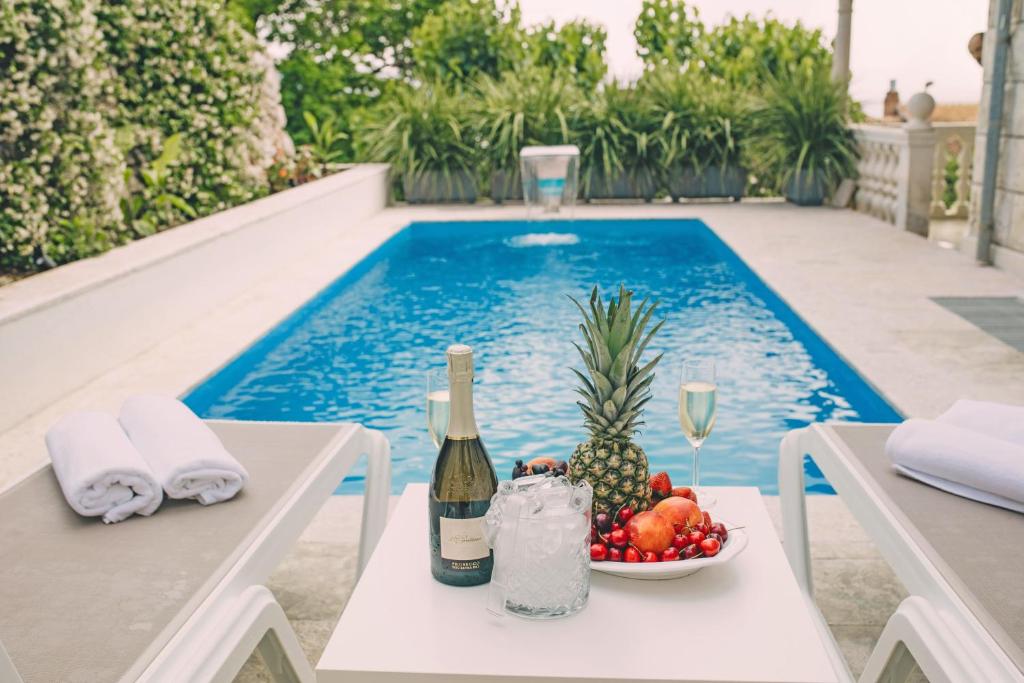 波尔Villa Ardura - island holiday residence **** Bol. Island Brač的游泳池旁的一瓶葡萄酒和一碗水果