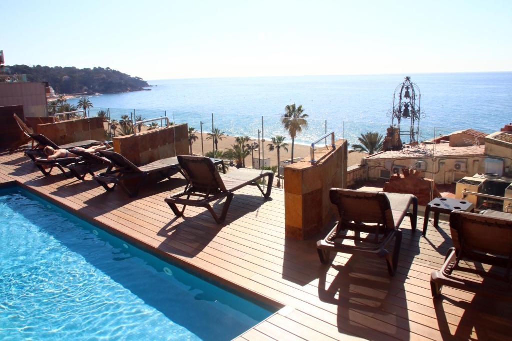 罗列特海岸Hotel Metropol的一个带椅子的甲板和一个毗邻大海的游泳池