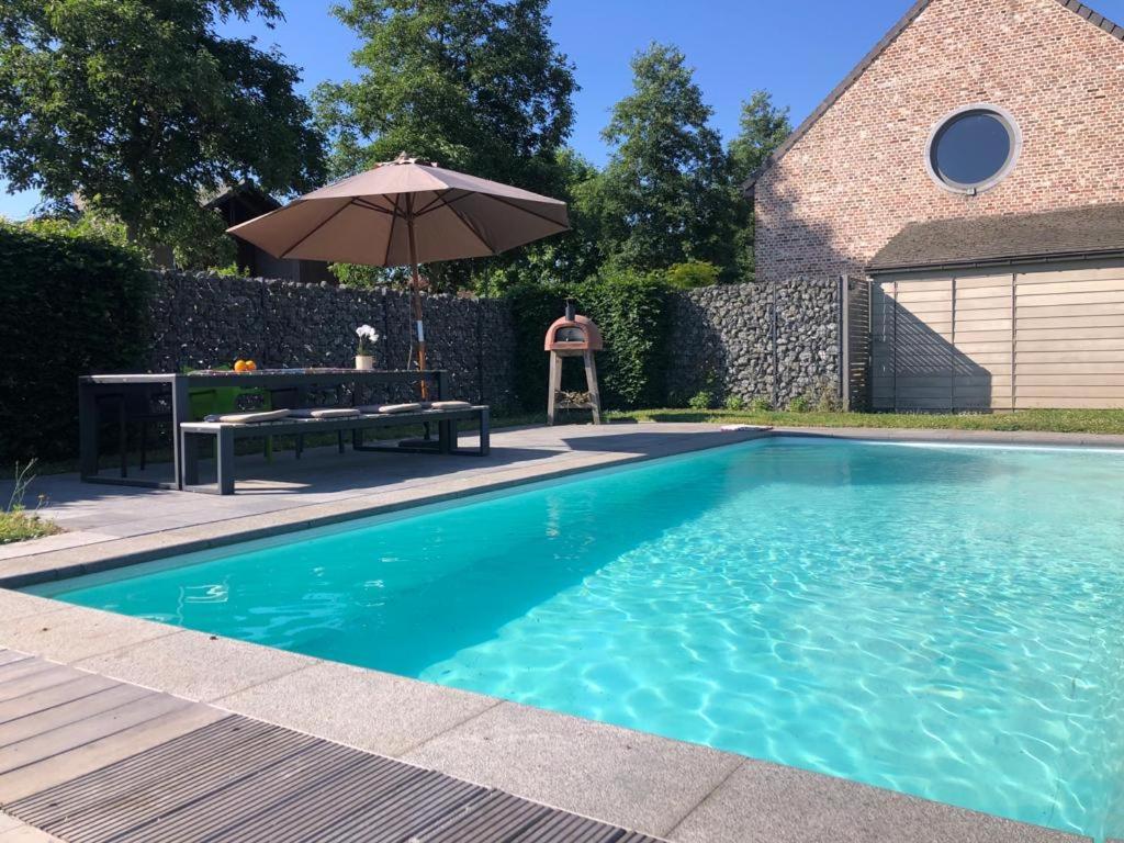 Zemstlandelijke villa met zwembad en gezellige openhaard的一个带桌子和遮阳伞的游泳池